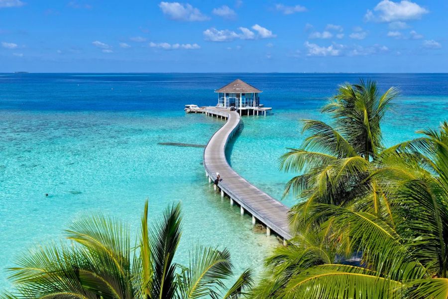 Sunny Maldives resort jetty beside a turquoise lagoon